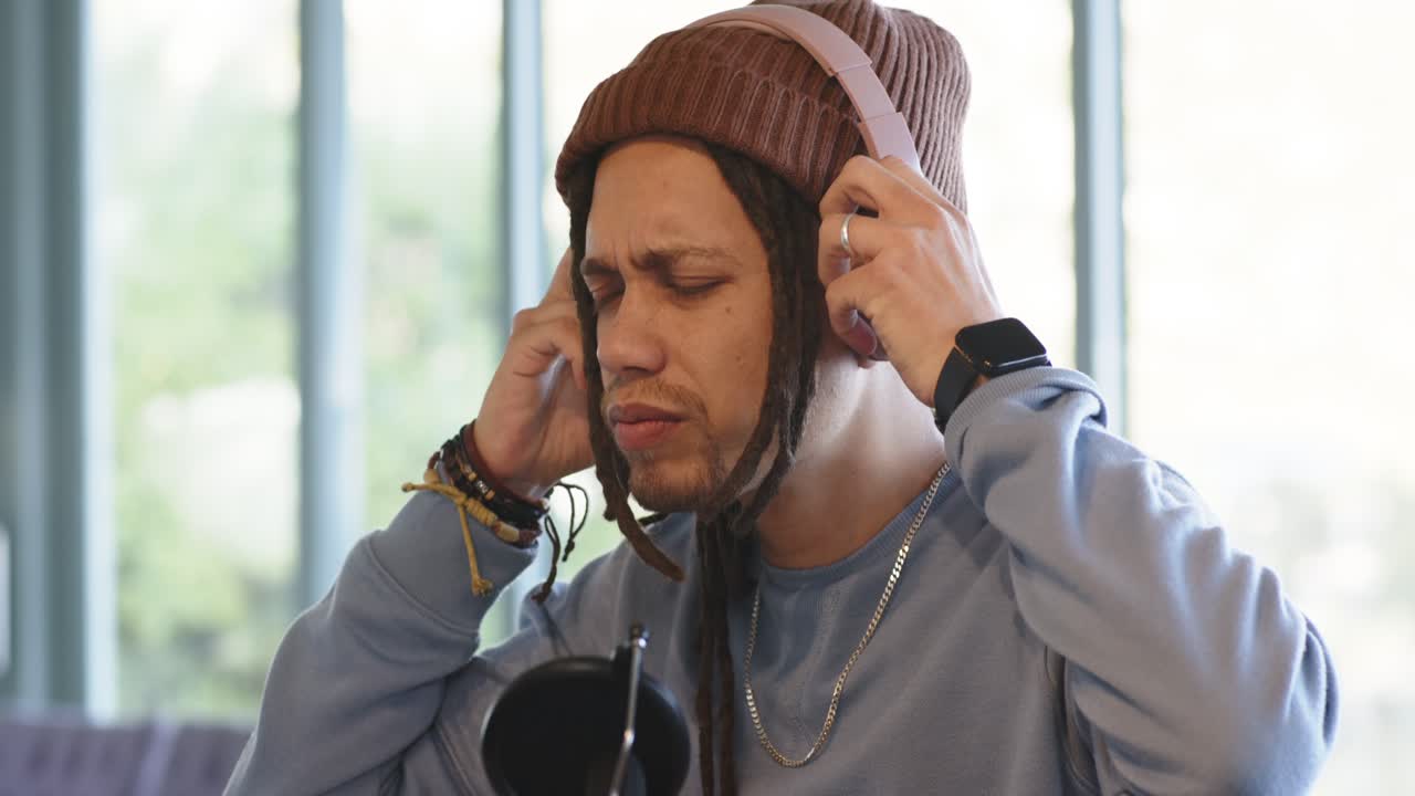 Seorang pria paruh baya mengangkat headphone, menyesuaikan bantalan telinga, dan mendengarkan sinyal uji di mikrofon studio rumah.