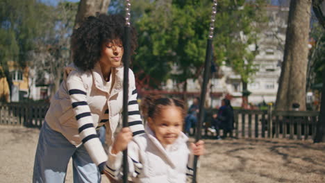 mother pushing swing daughter playing on playground. cute girl swinging.