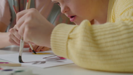 cheerful girl with down syndrome enjoying painting with teacher