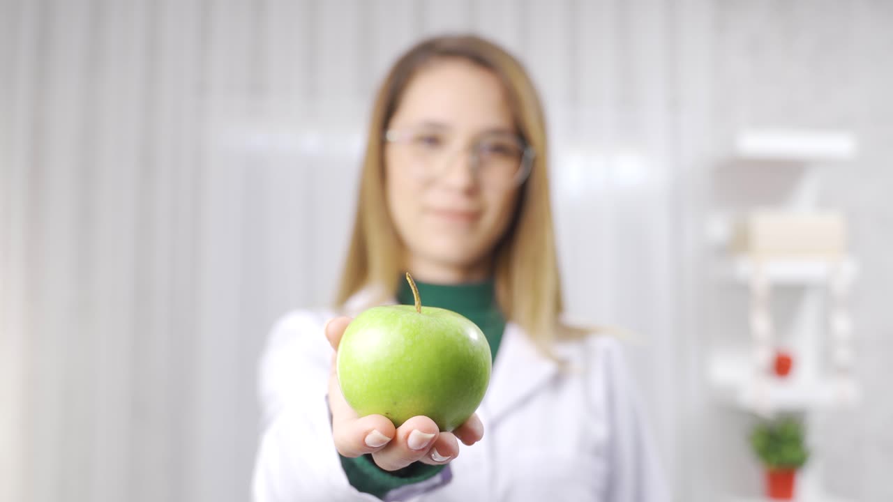 una experta en nutrición entrega una manzana verde orgánica a la cámara.