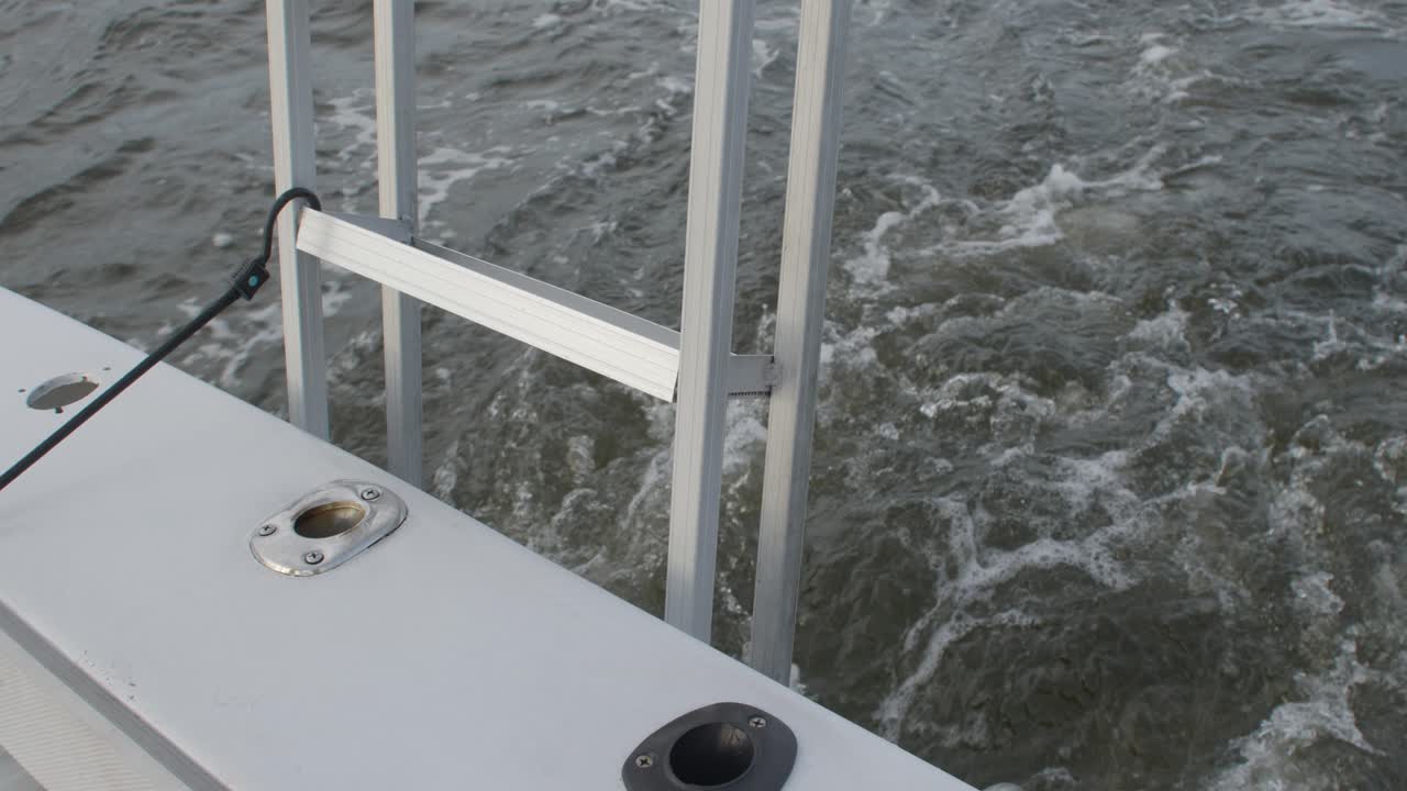 Rear view from a boat in motion as it cuts through choppy water, showing bubbling wake and stainless steel railing
