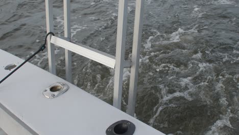 rear view from a boat in motion as it cuts through choppy water, showing bubbling wake and stainless steel railing