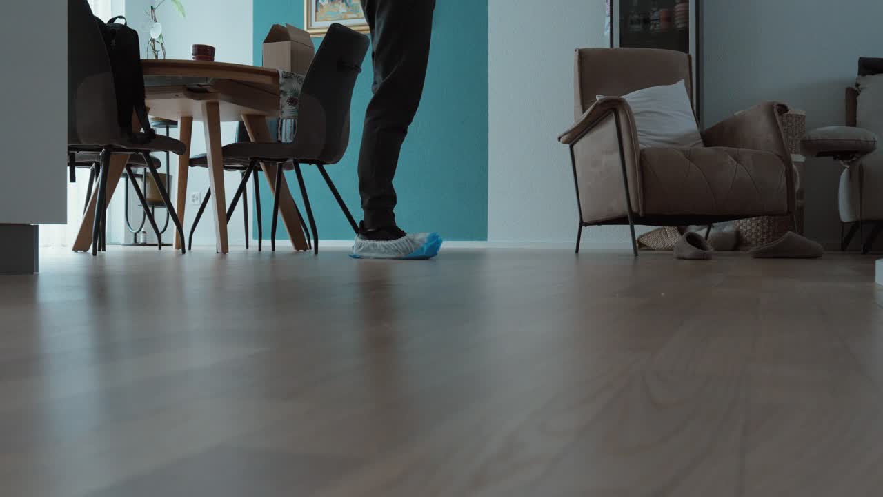 Foto en interiores tomada a un ángulo bajo de una persona caminando por un apartamento moderno con protectores de zapatos desechables azules, lo que sugiere un servicio profesional a domicilio y limpieza. Ideal para servicios de limpieza y mantenimiento.