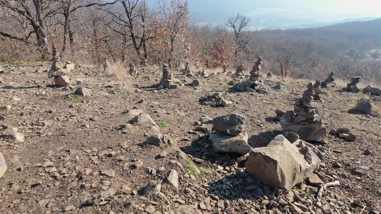 Tracking shot near Palm of God wooden tourist attraction during the day with handmade balancing rock towers on a hill, near Holloko, Hungary.