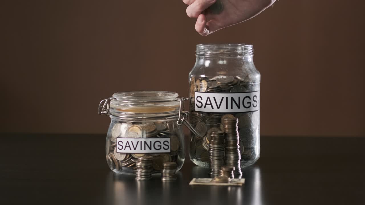 Hand of Man Putting Money into Glass with Savings