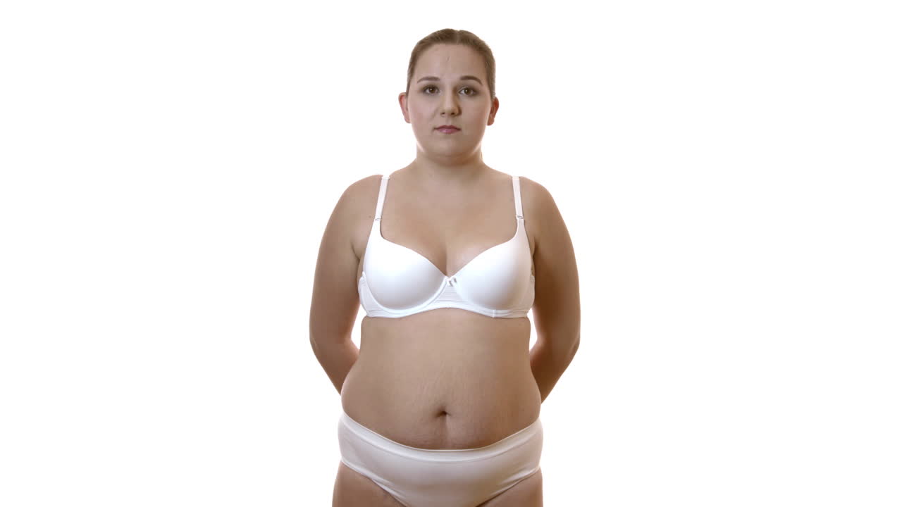 Oversized Woman Standing In Her Underwear With Arms Behind Her Back In A Studio With White Background - Medium Shot