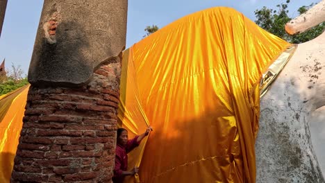 covering a large buddha statue with a golden cloth