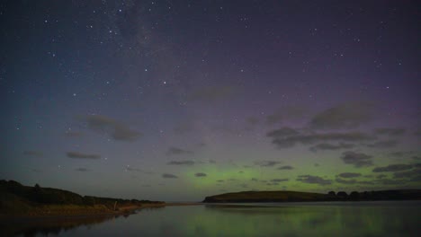 espectacular timelapse que captura la hermosa actividad auroral en el entorno costero de nueva zelanda, aurora australis con vibrantes verdes, rojos y morados que se muestran en el oscuro cielo nocturno con nubes en movimiento
