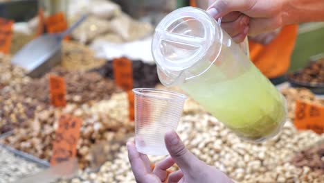 degustando limonada fresca en el bazar, vertiendo limonada a mano en un vaso de plástico de cerca