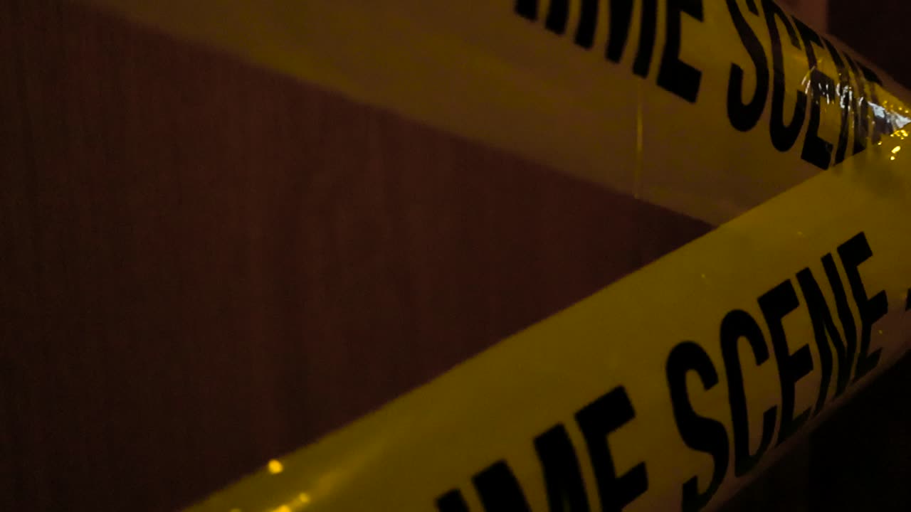 Close up or closeup footage moving closer to a yellow Crime Scene Do Not Enter police tapes that are crossed over each other in front of a wooden brown door in front of a apartment or house door