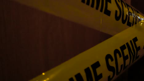 close up or closeup footage moving closer to a yellow crime scene do not enter police tapes that are crossed over each other in front of a wooden brown door in front of a apartment or house door