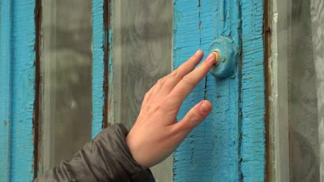 woman pressing the doorbell button on the old blue door 01