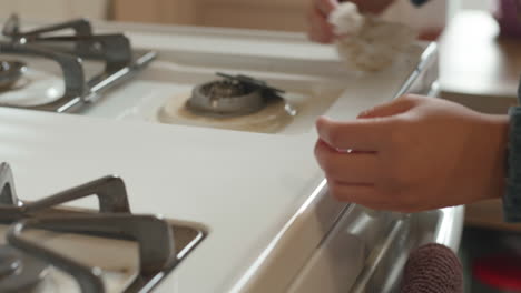 Close-up-of-female-hands-cleaning-old-gas-stovetop,-slow-motion