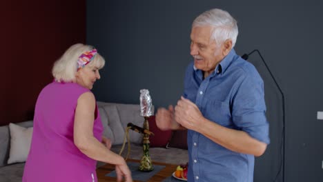 Feliz-Pareja-De-Ancianos-Bailando-Divirtiéndose-Celebrando-El-Aniversario-De-Jubilación-En-El-Salón-De-Casa