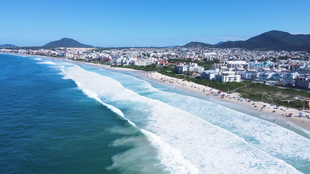 Panoramic aerial view of Ingleses beach in Florianópolis, Santa Catarina, crowded with people and umbrellas during the peak summer season with turquoise blue sea