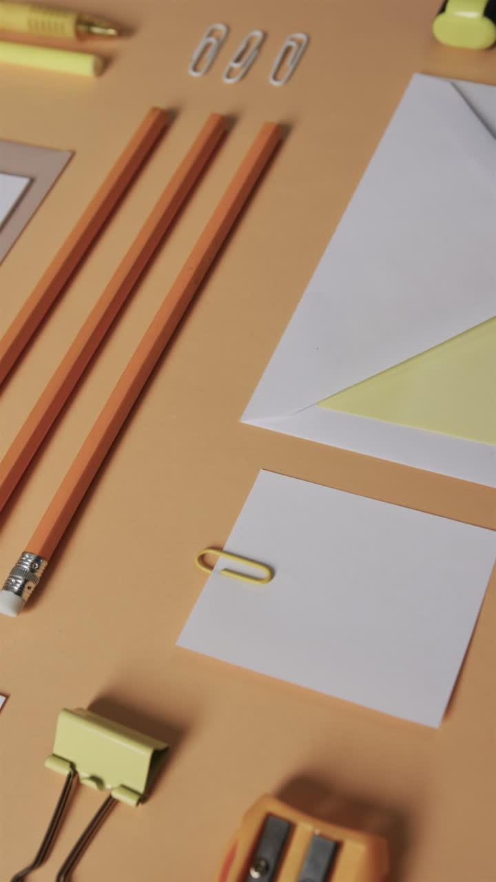 Vertical video of close up of pencils and stationery arranged on beige background, in slow motion