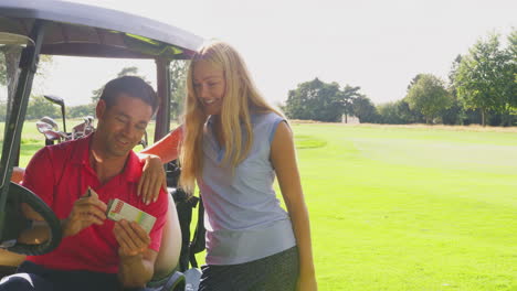 couple playing round on golf together sitting in buggy with score card