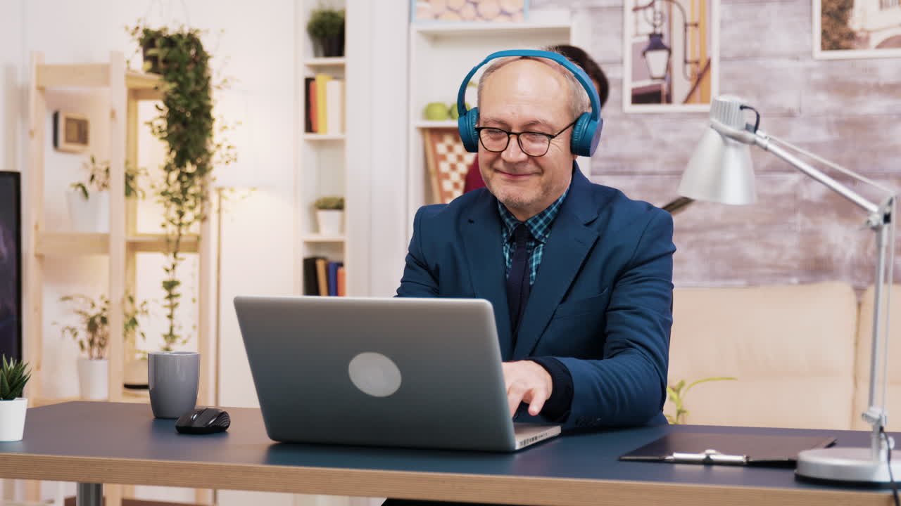 Senior Man Working From Home With Laptop And Headphones