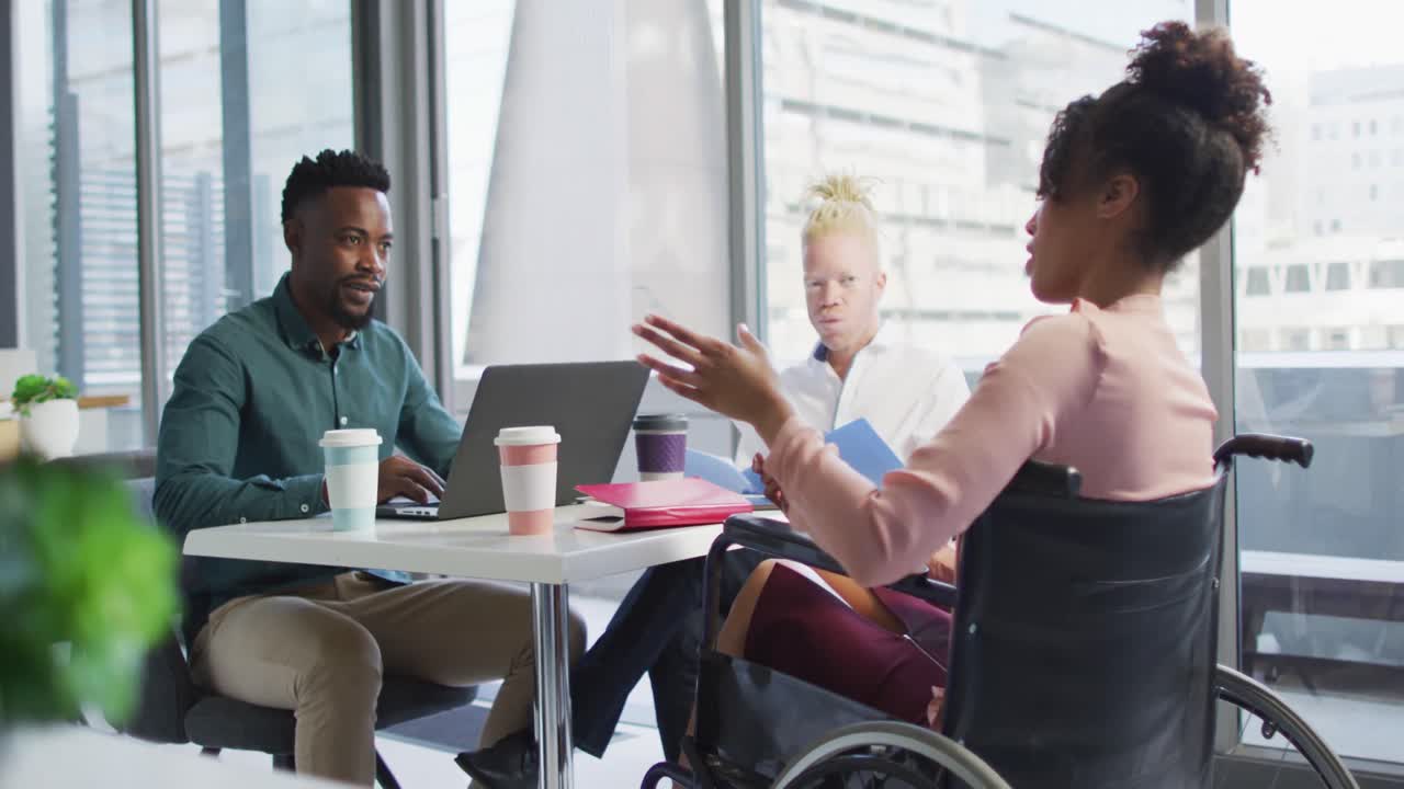 Diverse business people discussing with disabled colleague and documents in creative office