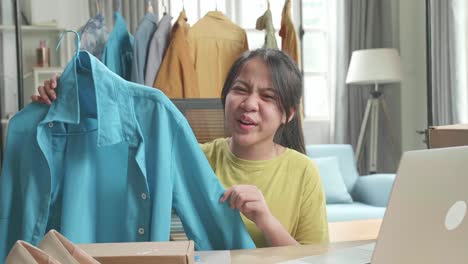 asian young girl online seller recommending a shirt while using computer for selling clothes at home