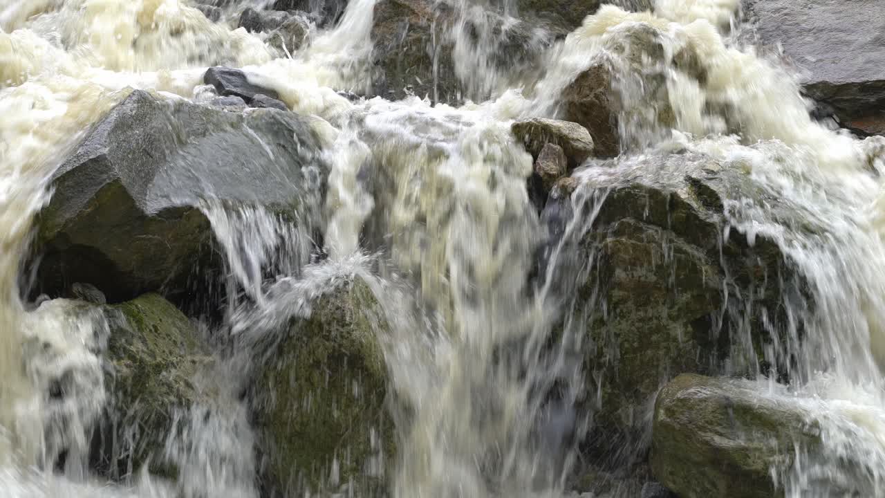 Brown flood water pouring over rocks during heavy rain and flooding - Closeup detail