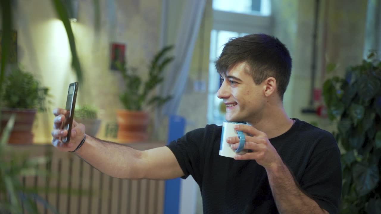 Giovane studente europeo si sta scattando un selfie mentre gusta il suo caffè o tè in caffetteria con uno sfondo naturale.