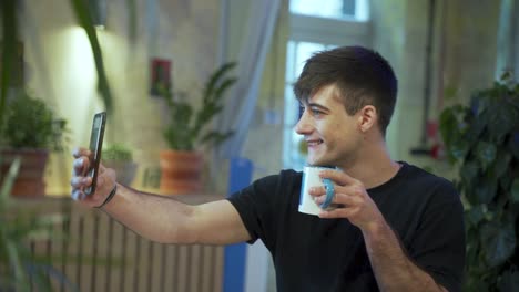joven estudiante europeo se está tomando selfie disfrutando de su café o té en la cafetería con un fondo natural