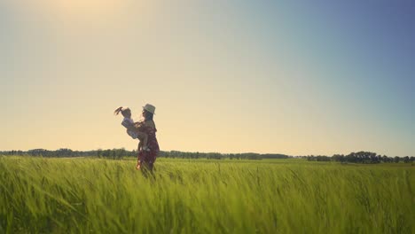 Cámara-Que-Sigue-A-Mamá-En-El-Campo-Y-Usa-Gafas-De-Sol-Sostiene-A-Su-Pequeña-Hija-En-Sus-Brazos-Con-El-Cabello-Y-El-Vestido-Revoloteando