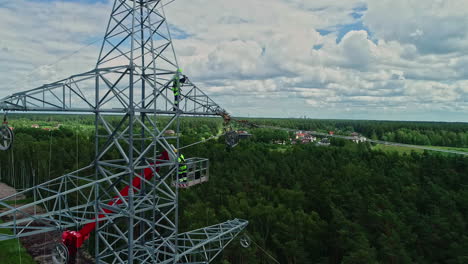 aerial view of two worker repairing or installing transmission tower in forest during cloudy day - close up