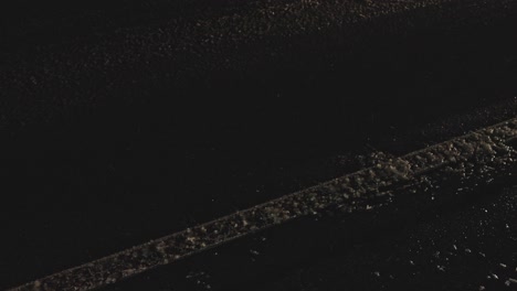 shot of wheels of slowly passing cars on wet road during night snowfall