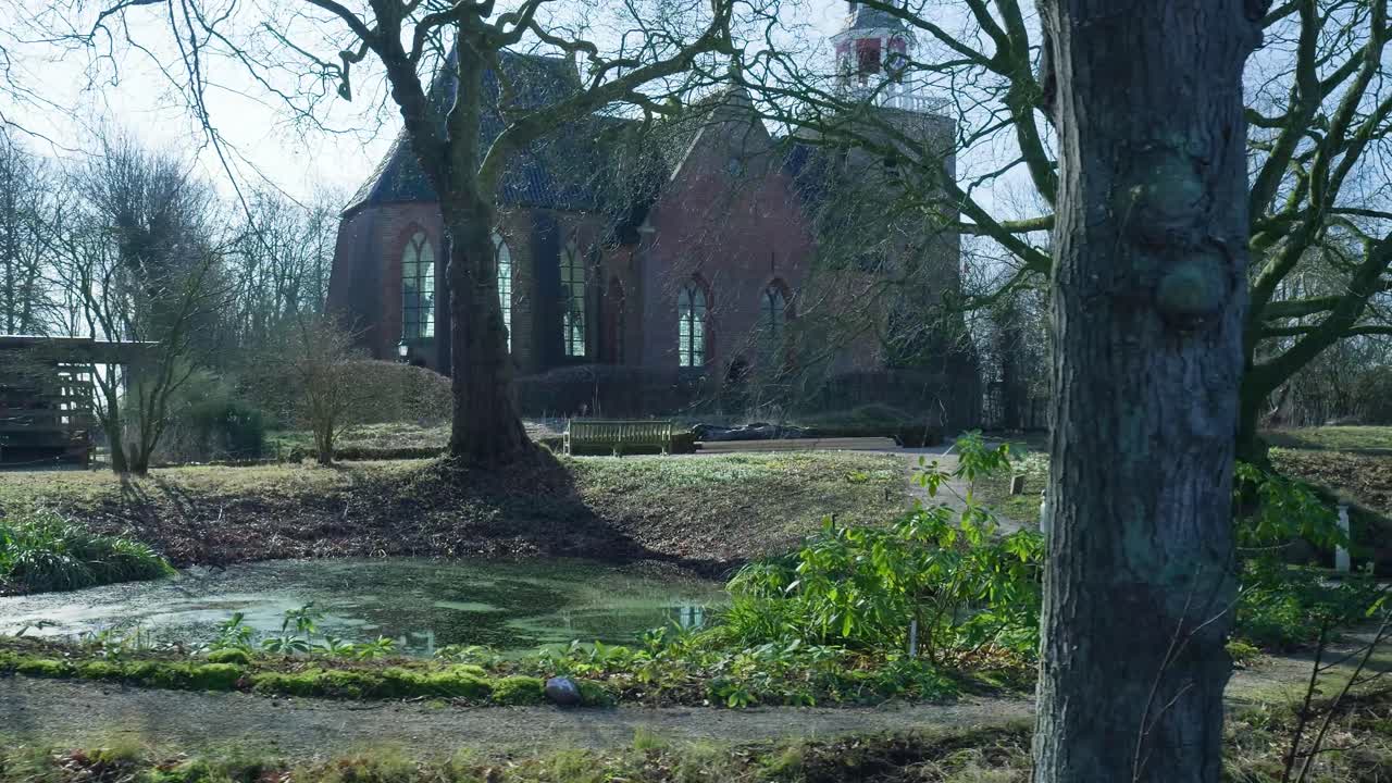 Historisk murstenskirke omgivet af nøgne træer og grønt løv