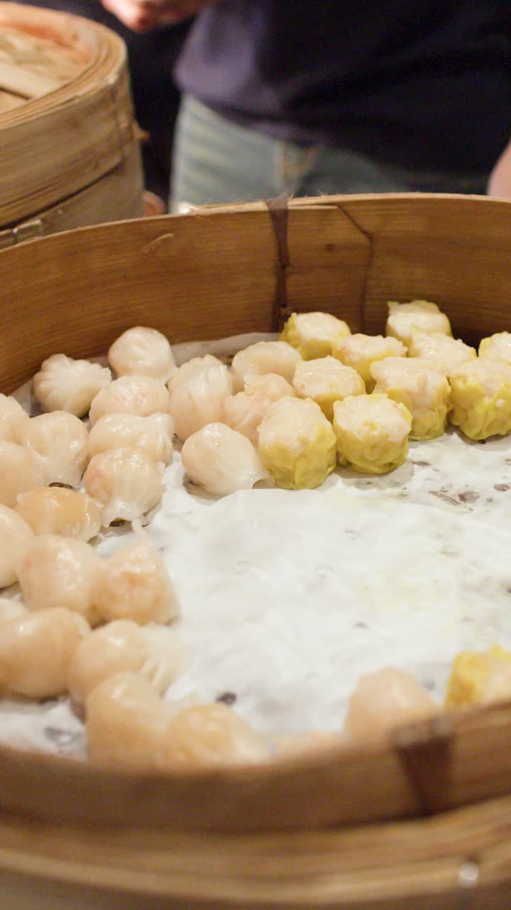 A person uses metal tongs to select shrimp and pork dumplings from a bamboo steamer