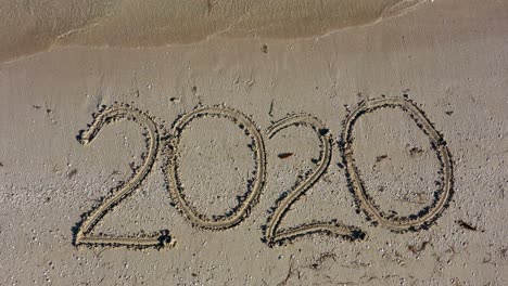 twenty twenty written in the sand and filling the frame as water laps onto the beach