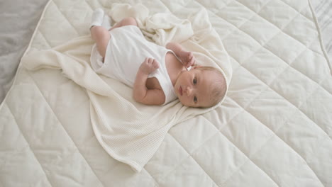 top view of a baby in white bodysuit lying on bed moving his legs and arms