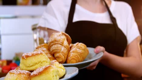 camarera sosteniendo un plato de croissant y comida dulce