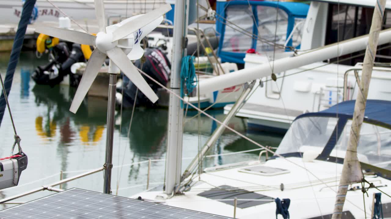 Small wind turbine rotates on docked sailboat, overcast lighting, steady camera, marina background