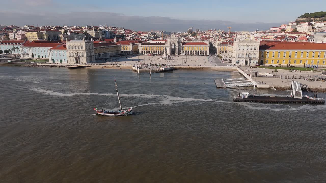 Ripresa aerea con allontanamento mentre l'acqua del fiume Tago scorre e una barca a vela si avvicina davanti a una piazza a Lisbona, Portogallo.