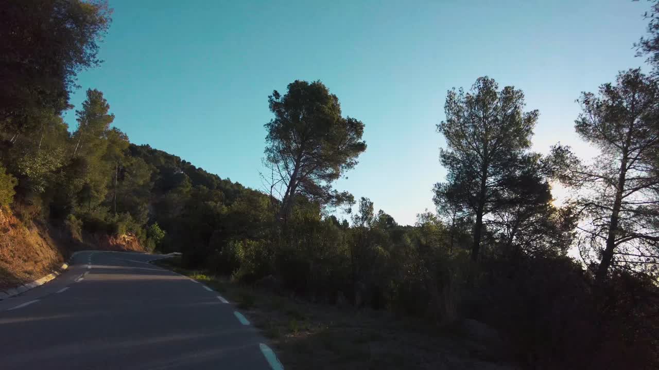 Driving on a mountain road surrounded by vegetation and trees, during the sunrise at early morning, view from the car