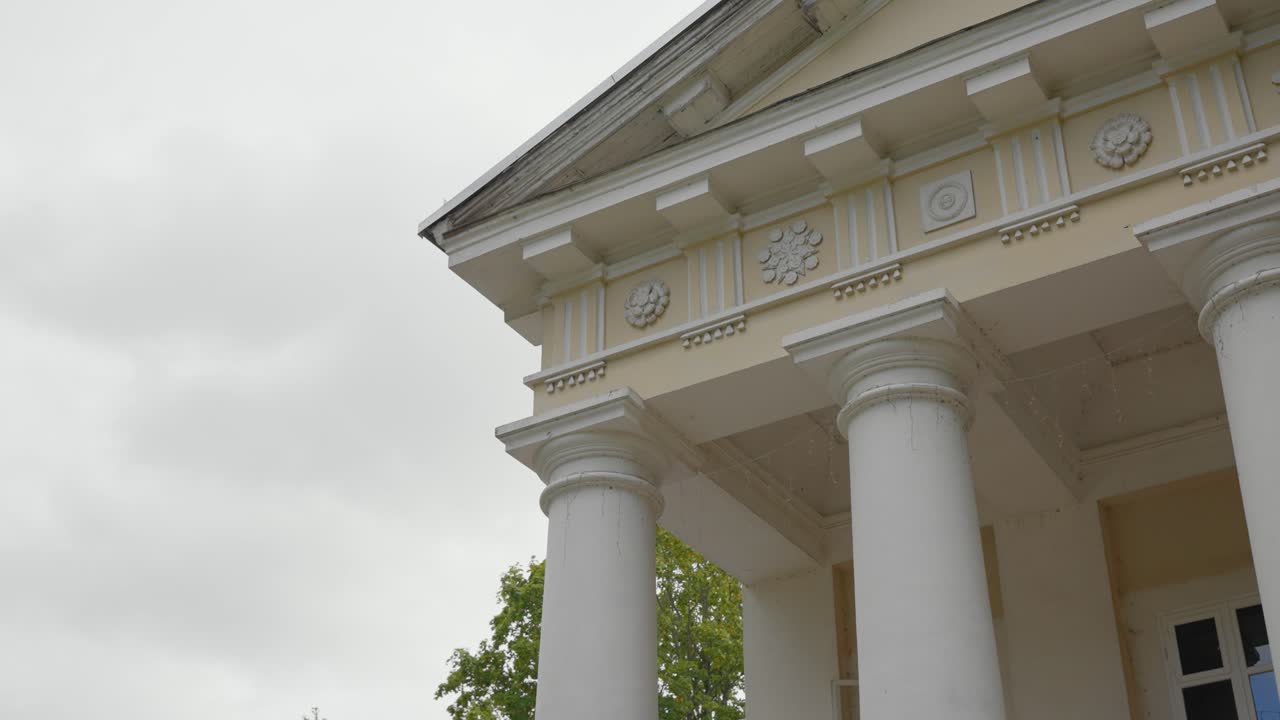 Elegante facciata di edificio neoclassico che mostra colonne dettagliate e fregi decorativi. Il cielo coperto fornisce un'illuminazione diffusa, evidenziando la complessità architettonica.