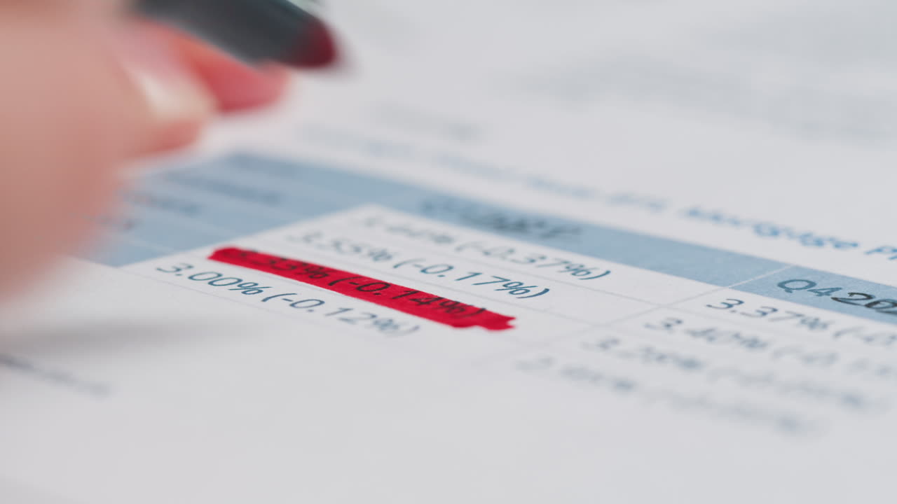 Hand Highlighting Financial Data on a Report with a Red Marker