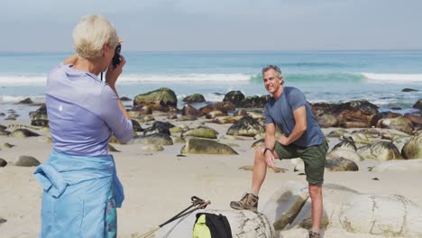 una mujer excursionista senior tomando fotos de un hombre excursionista senior usando una cámara digital en la playa.
