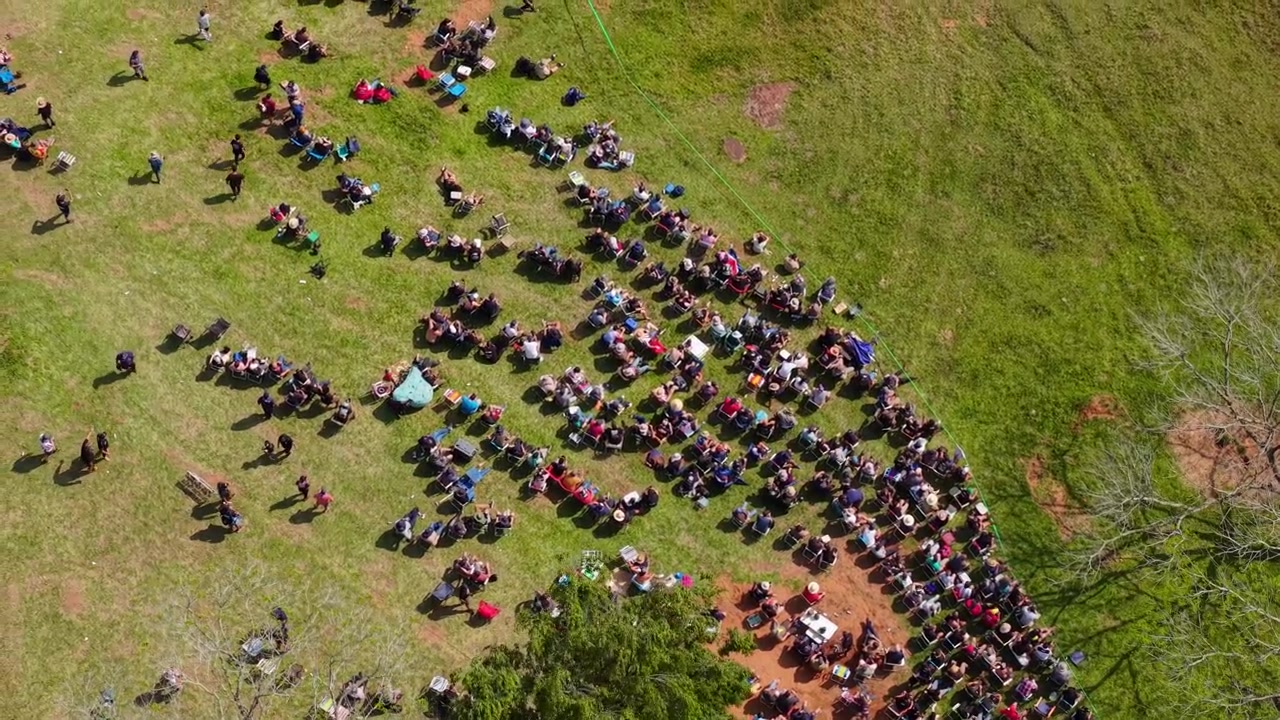 Camping Rally 2026 spectators gather beside the rally stage in Nueva Alborada, Itapua, Paraguay, South America, forming a large crowd along the rural course, top-down drone forward flyover.