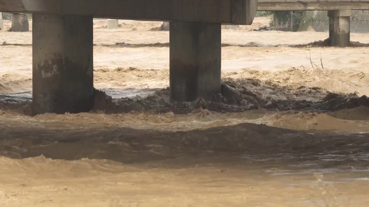 Água de enchente lamacenta correndo sob pilares de ponte de concreto