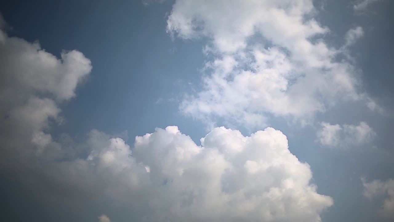 Puffy fluffy white clouds slowly moving in the clear blue sky, static shot