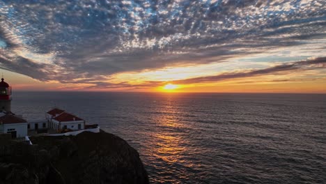 aerial shot of cabo de são vicente lighthouse at sunset, with the sun casting golden hues over the ocean.