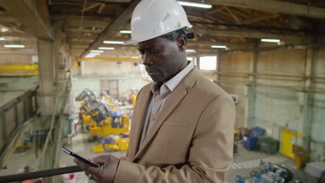 african american engineer using smartphone in factory