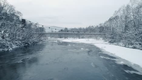 drone view of frozen river, swimming wild ducks, hanging bridge in winter morning