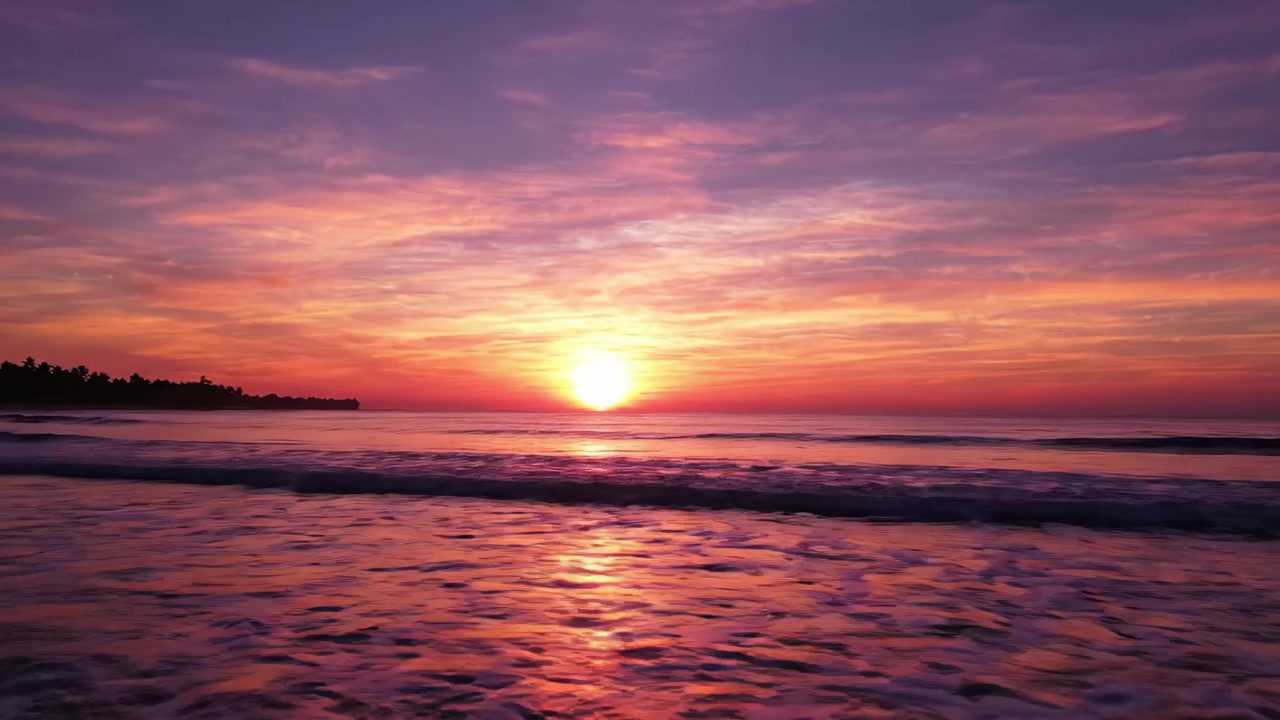 Betagende solnedgang over rolige vande: Et fredfyldt øjeblik, når solen dykker ned under horisonten, badet i levende nuancer af lilla, pink og orange, der spreder sig over himlen