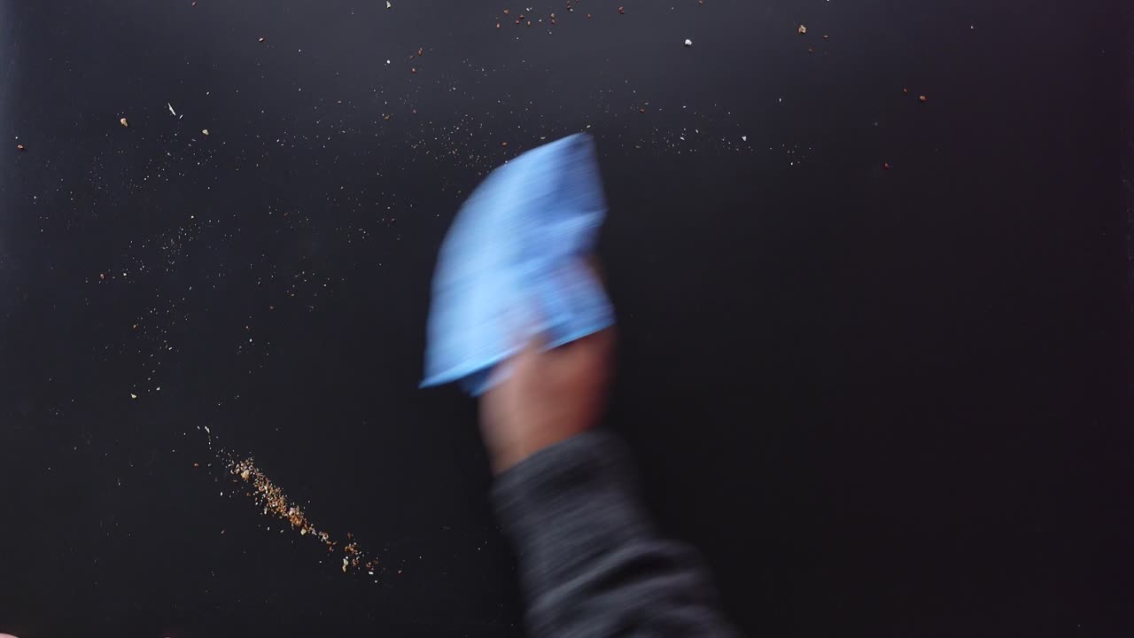 persona limpiando una superficie negra con un paño azul
