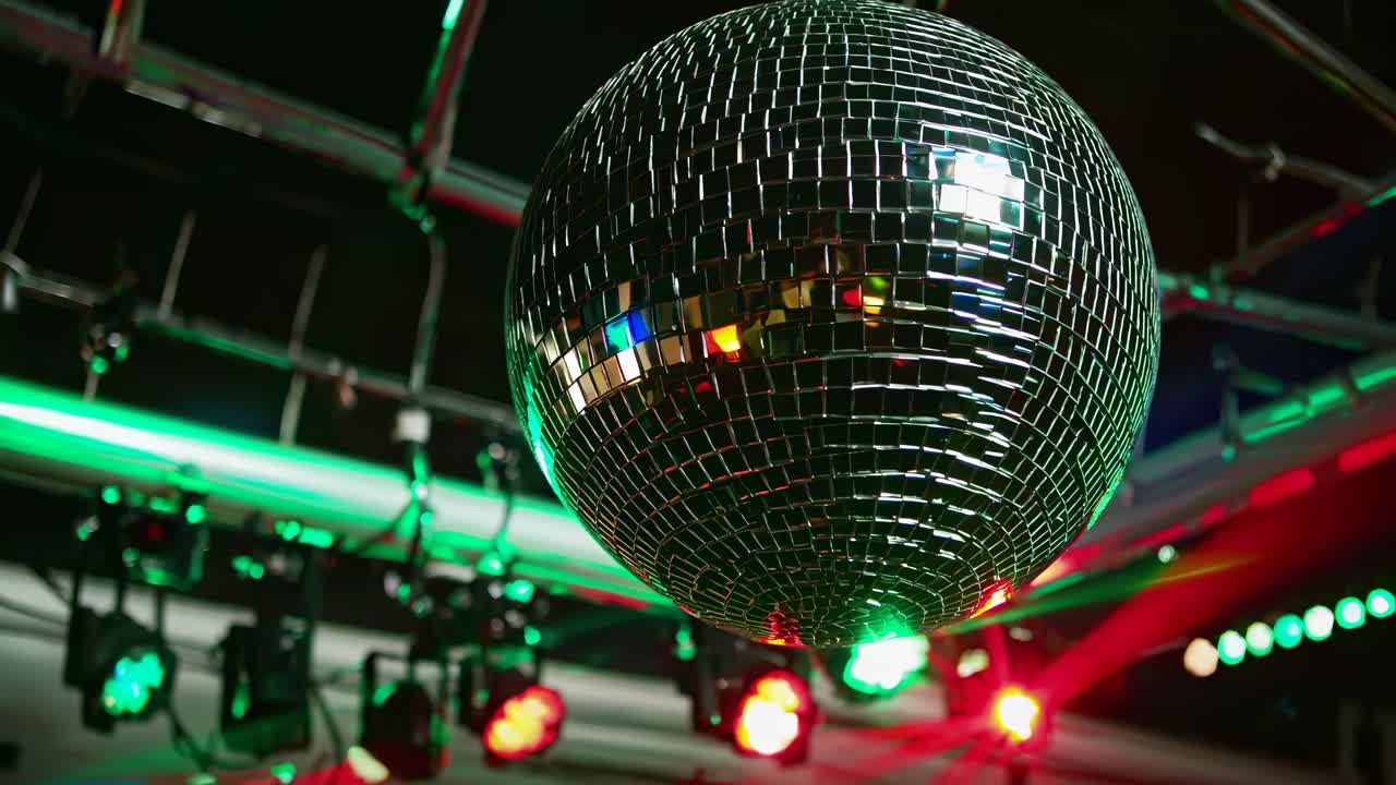 Primo piano di una palla da discoteca che riflette luci colorate in una stanza scarsamente illuminata, ripresa dal basso.